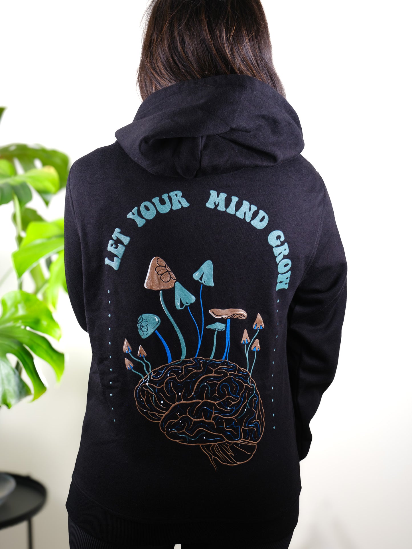 Female model back view with Let Your Mind Grow hoodie, showcasing nature, psychedelic, and mushroom-themed tattoo art.