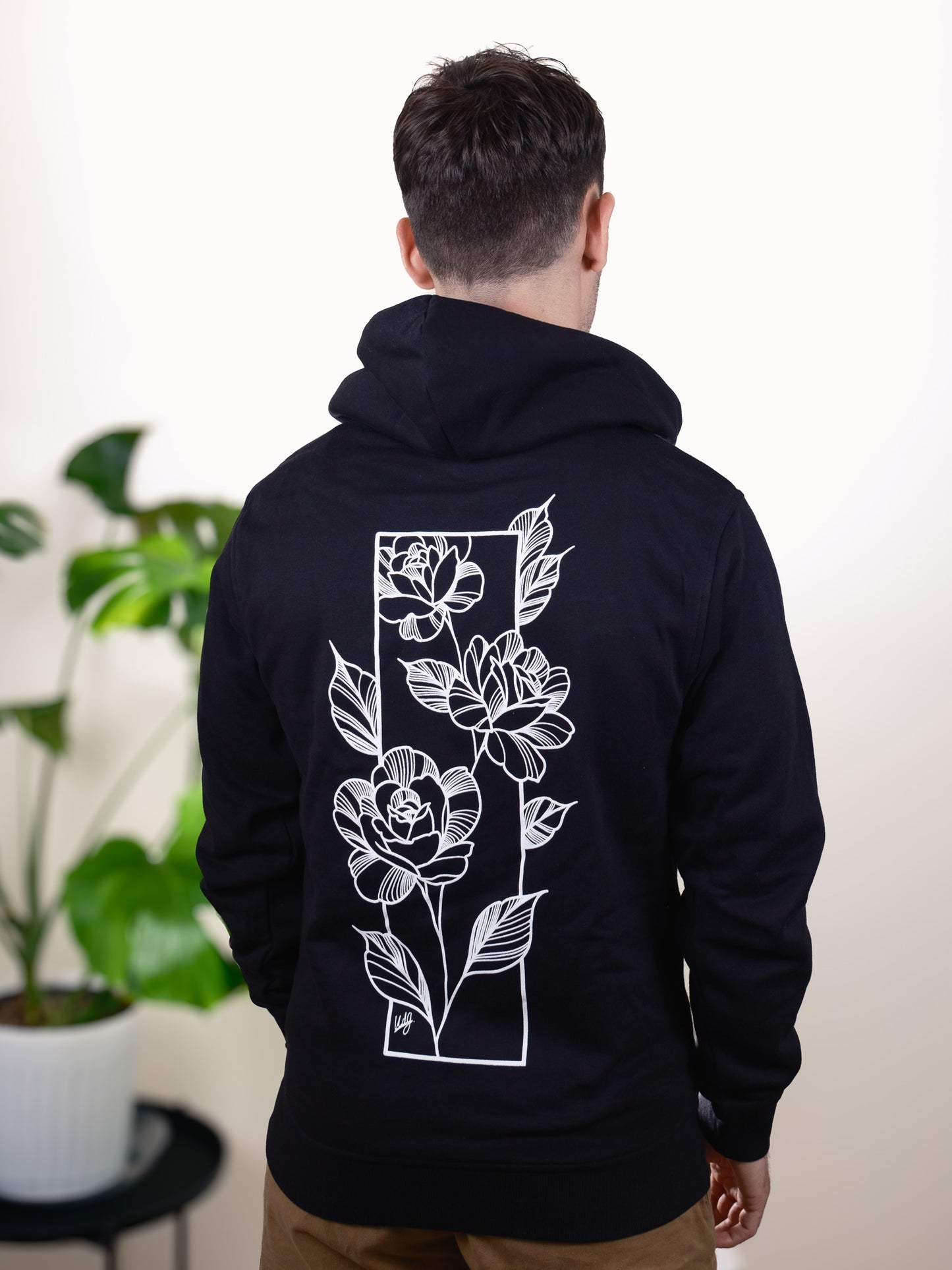 Male model wearing Love Knows No Bounds hoodie, back view with bold heart and floral tattoo-inspired design.
