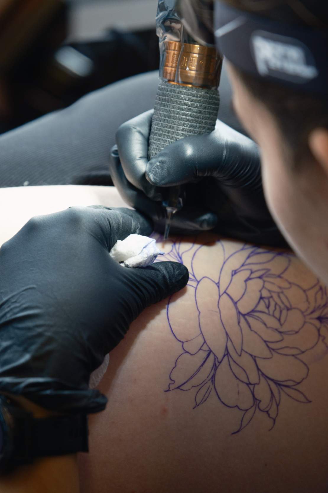 Close-up of tattoo artist Kansinee performing delicate line work on a fine line floral tattoo, showcasing precision and artistic skill.