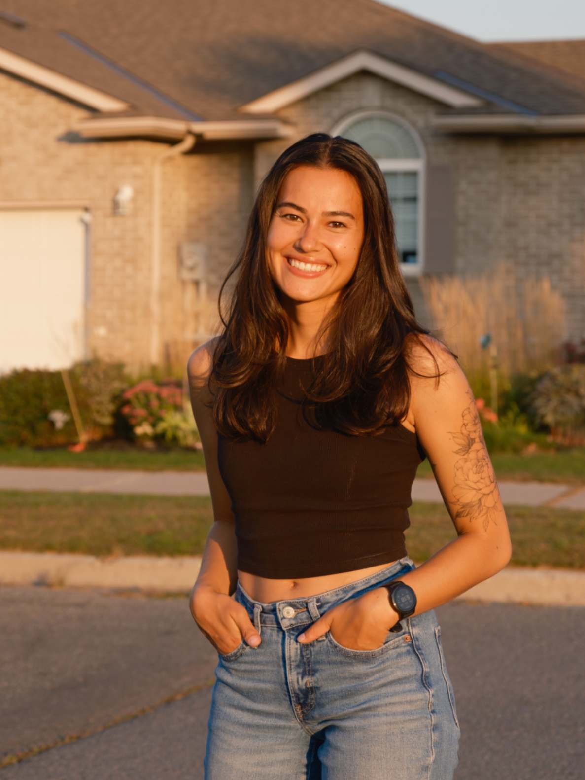 Kansinee, tattoo artist, smiling and greeting in a tank top, showcasing her floral arm tattoos.