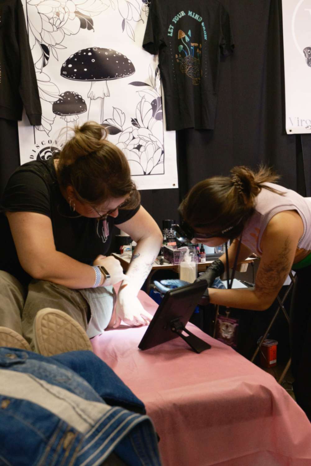 Kansinee at a tattoo convention showing a female client the stencil for their fine line floral tattoo, illustrating the consultation process.