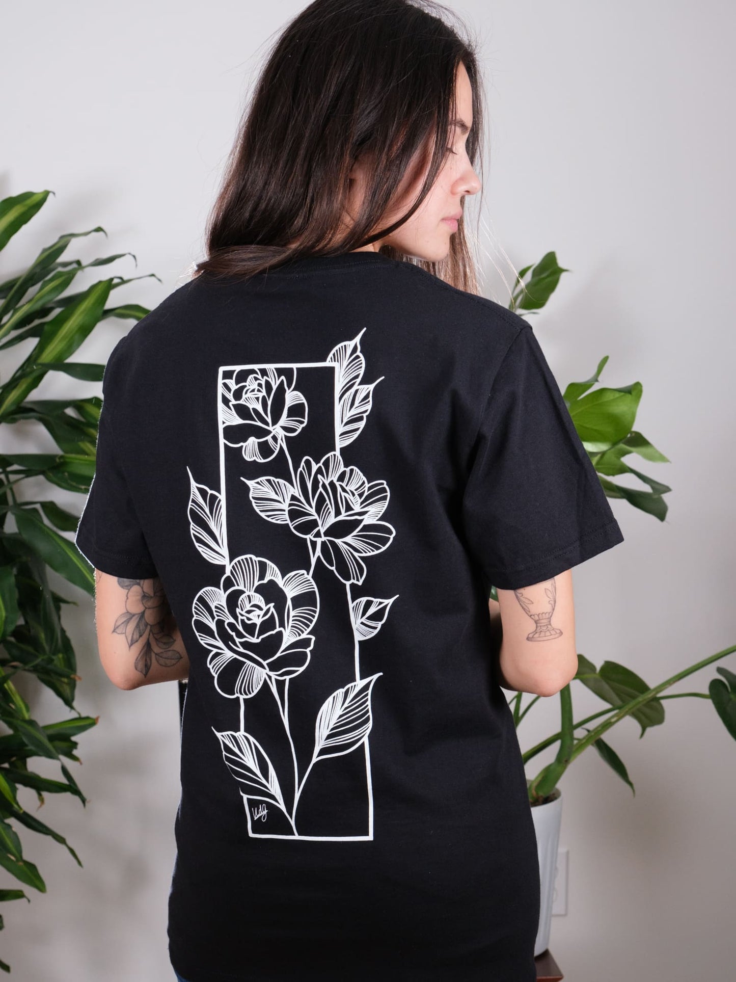 Female model displaying the back of the Love Knows No Bounds Black Tee, highlighting the intricate floral and rose artwork.