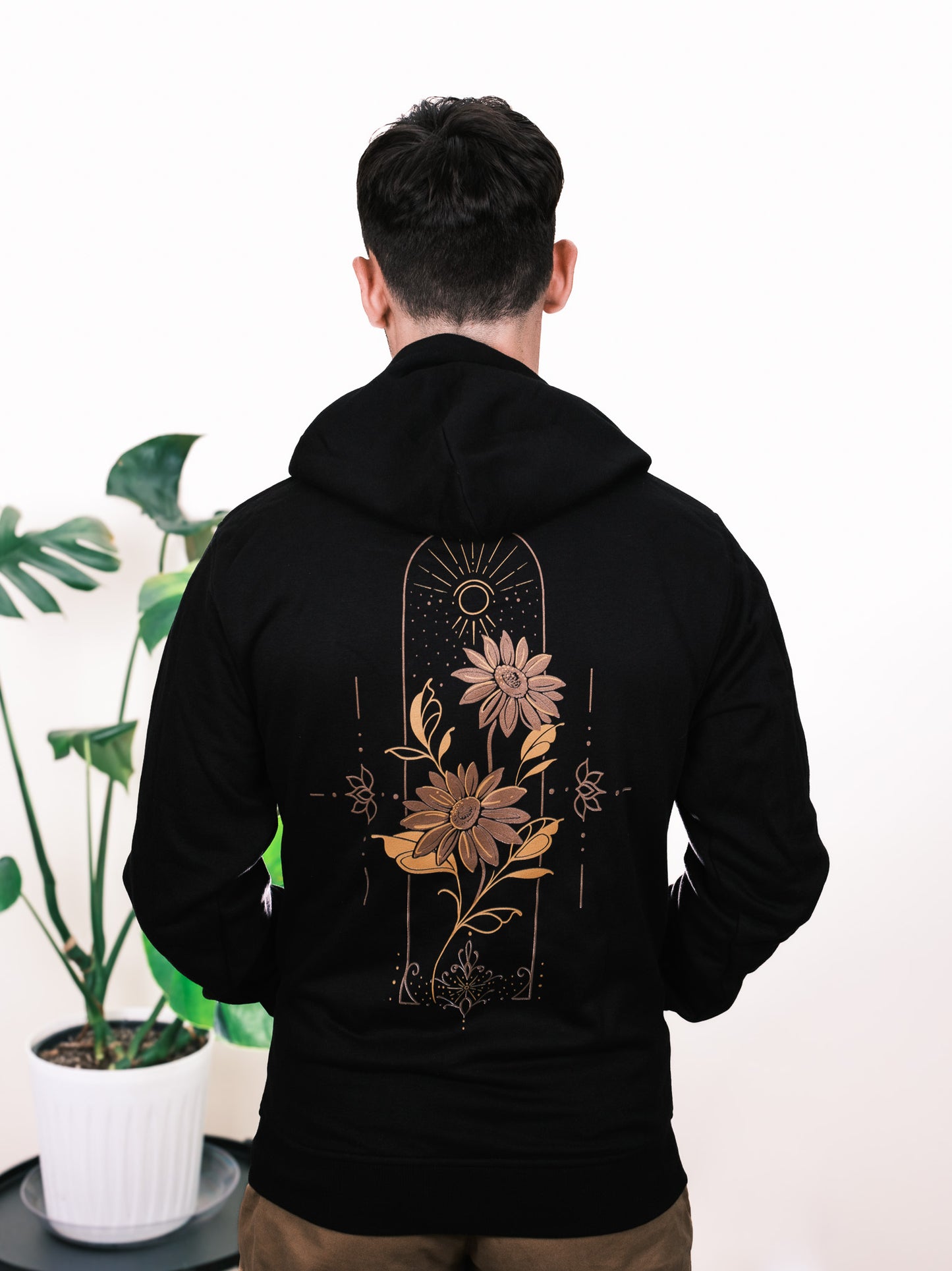 Male model wearing Follow the Sun hoodie, back view featuring vibrant sunflower design with fine line detailing
