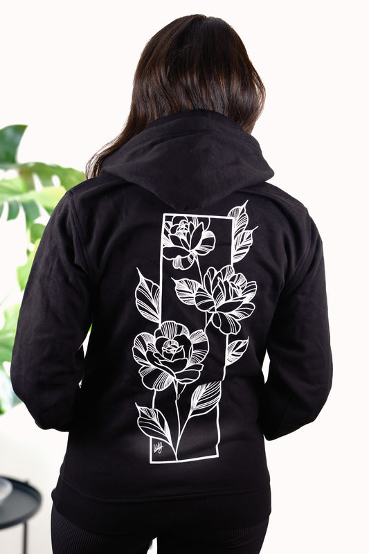 Female model wearing Love Knows No Bounds hoodie, back view featuring heart and floral design inspired by fine line tattoo art.