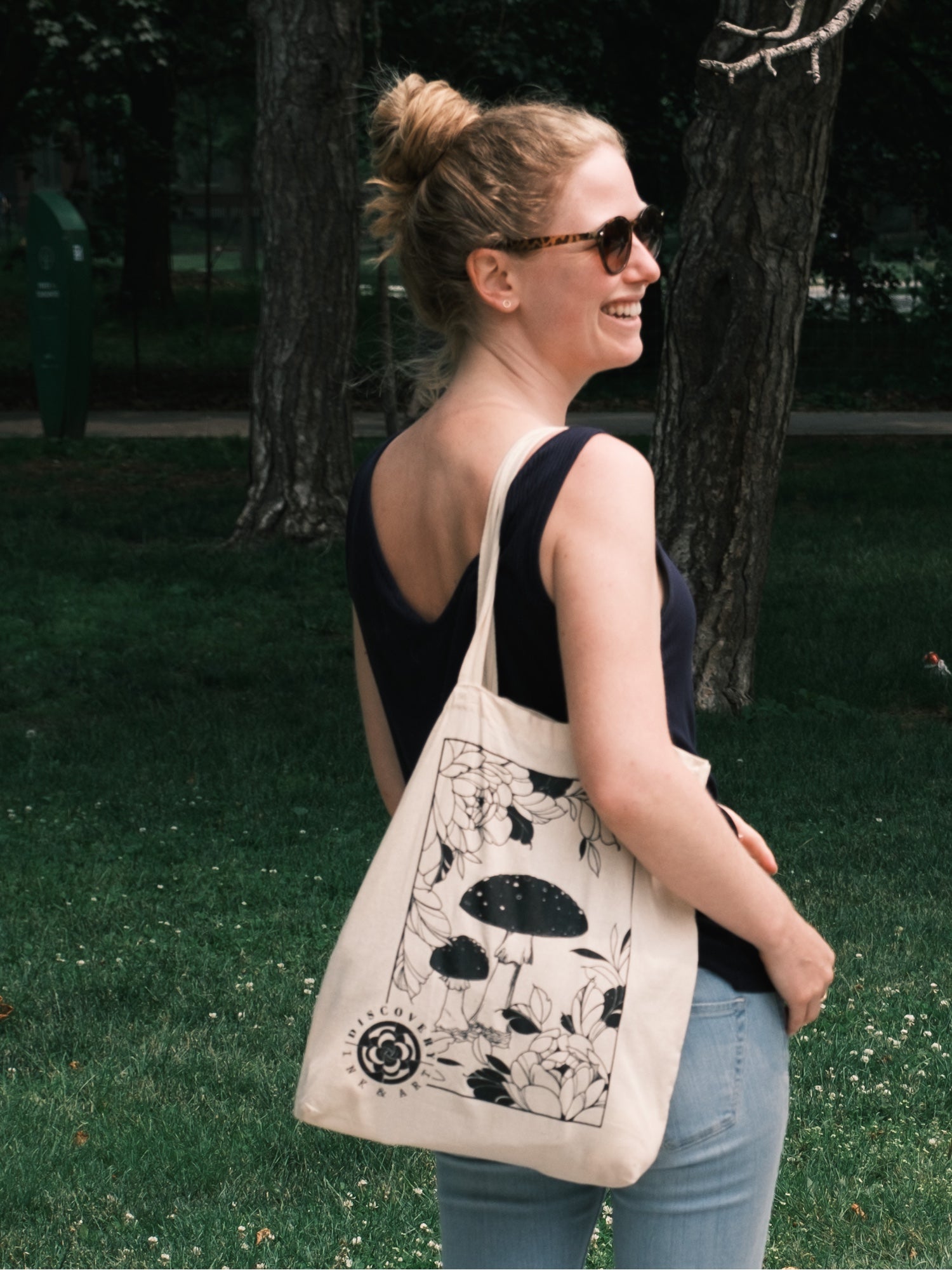Amanita Muscaria Mushroom surrounded by intricate botanicals and tattoo-inspired florals on a beige tote bag. Carried by smiling model