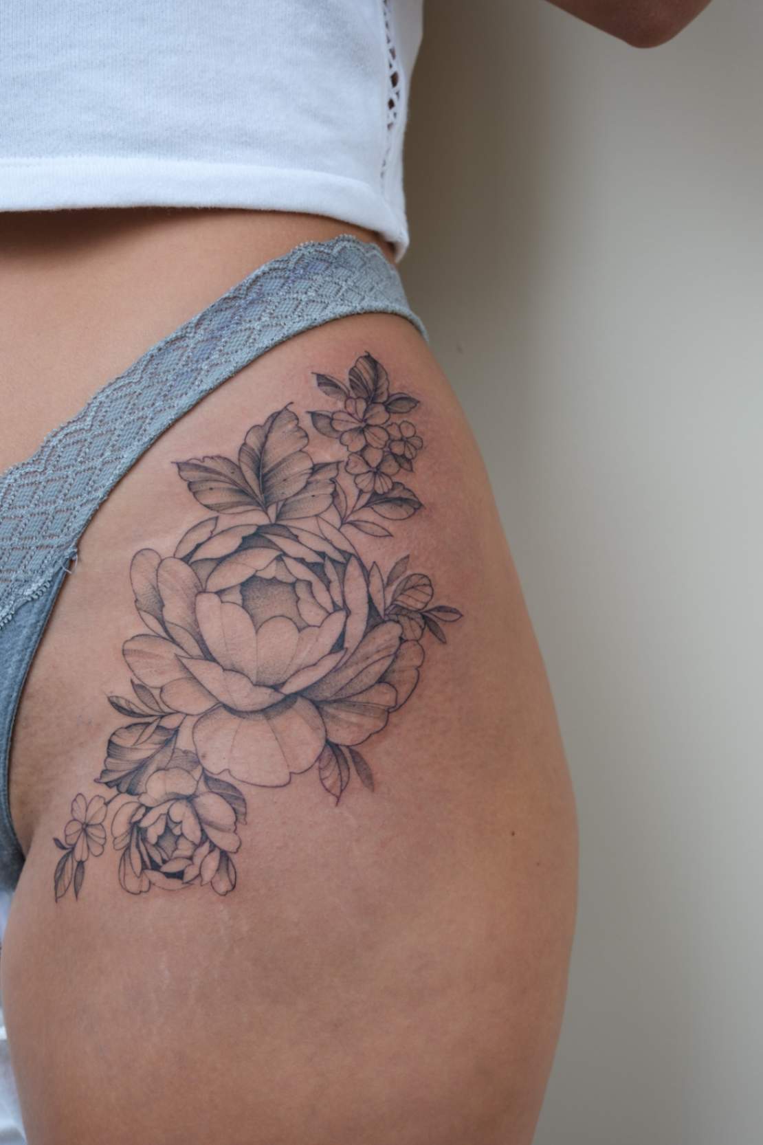 Fine line floral tattoo on a woman's hip, showcasing intricate and delicate floral designs.