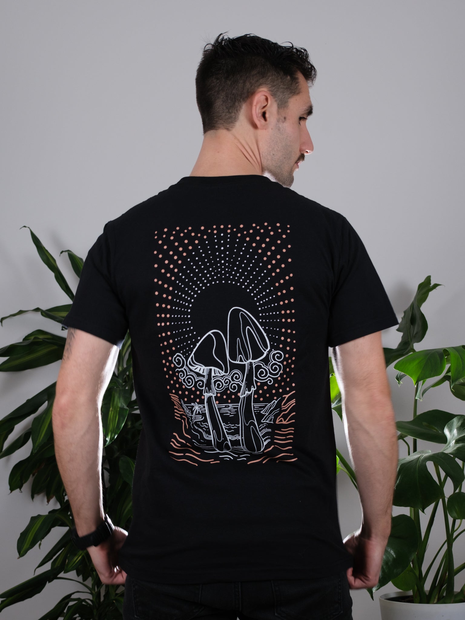 Back view of the Transcendent Love Tee on a male model, featuring a detailed psychedelic mushroom and pacific coast beach design.
